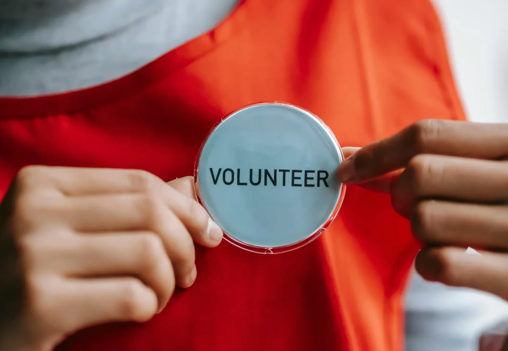 volontaria che tiene un badge con la scritta “VOLUNTEER”, simbolo di inclusione, partecipazione e impegno nella comunità.